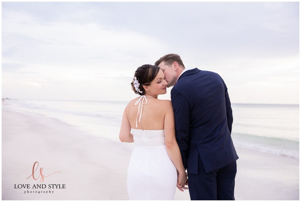Groom kissing brides forehead on the beach after their Anna Maria Island wedding ceremony 