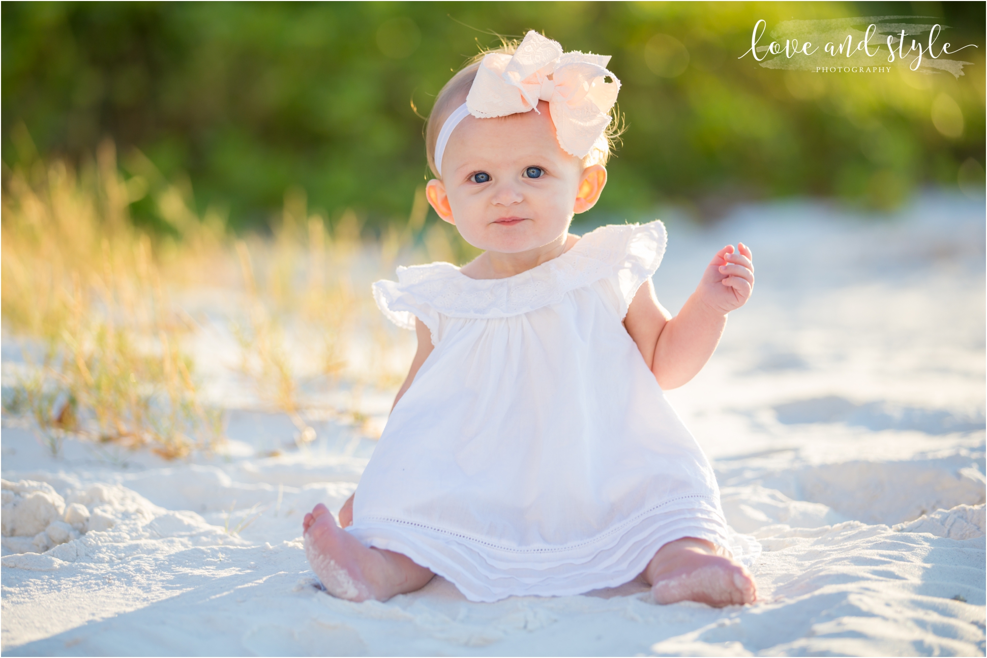 Baby on the beach wearing a white dress with a big white bow