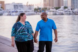 Sarasota Engagement Photographer of couple holding hands and walking with downtown Sarasota behind them