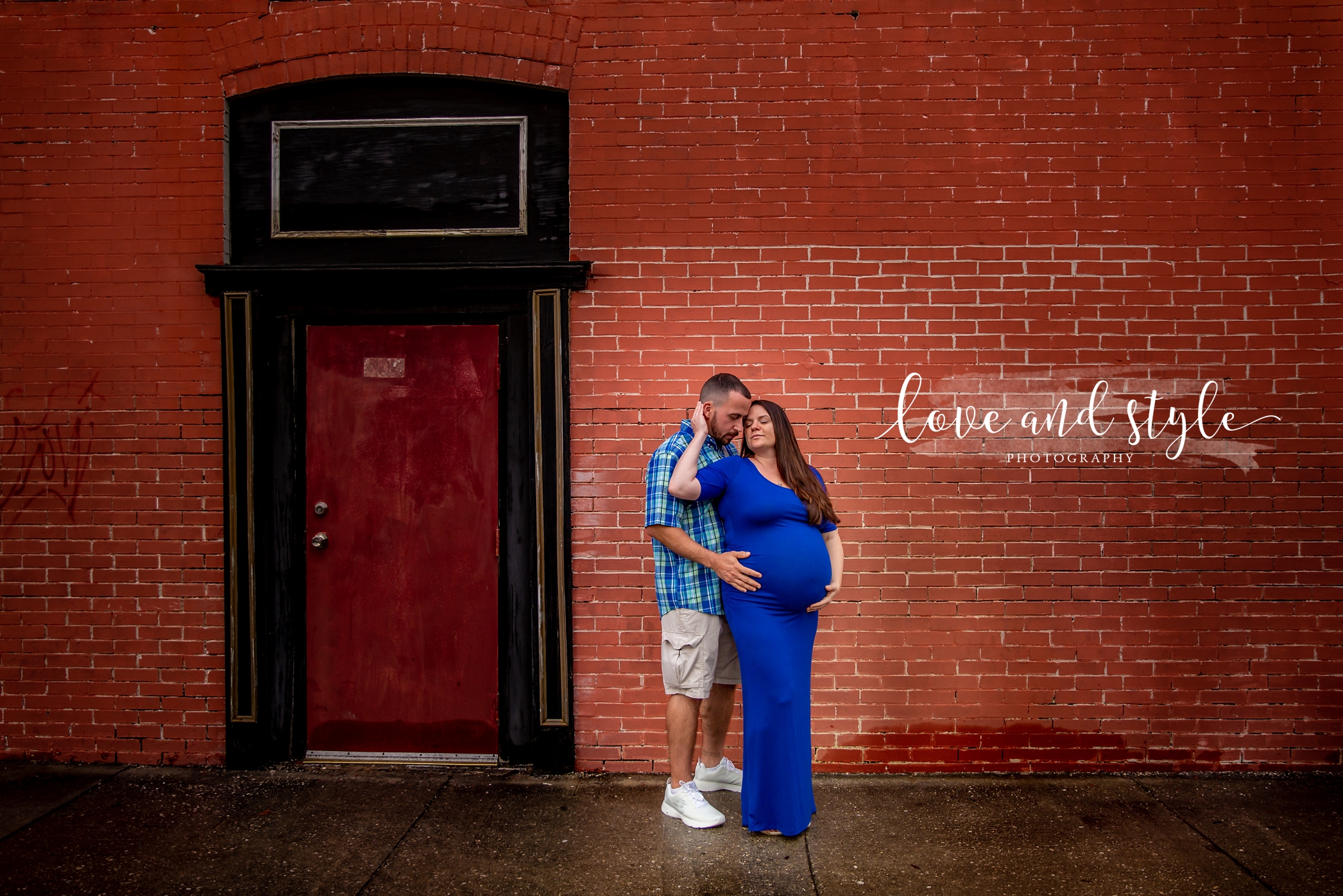 Downtown Bradenton maternity Photography of couple wearing blue embracing in front of a red brick wall