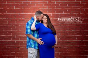 Downtown Bradenton maternity Photography of couple wearing blue embracing in front of a red brick wall