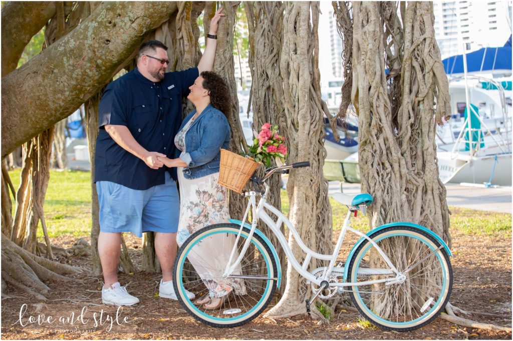 Engagement Photographer Sarasota with couple posed under a tree with a blue beach cruiser bike
