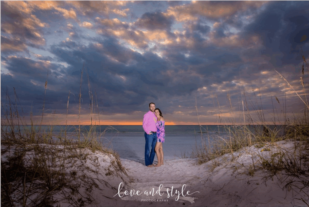 Engaged couple posing on the sand dunes during a Sarasota engagement photoshoot with a colorful sunset sky by Love and Style Photography.